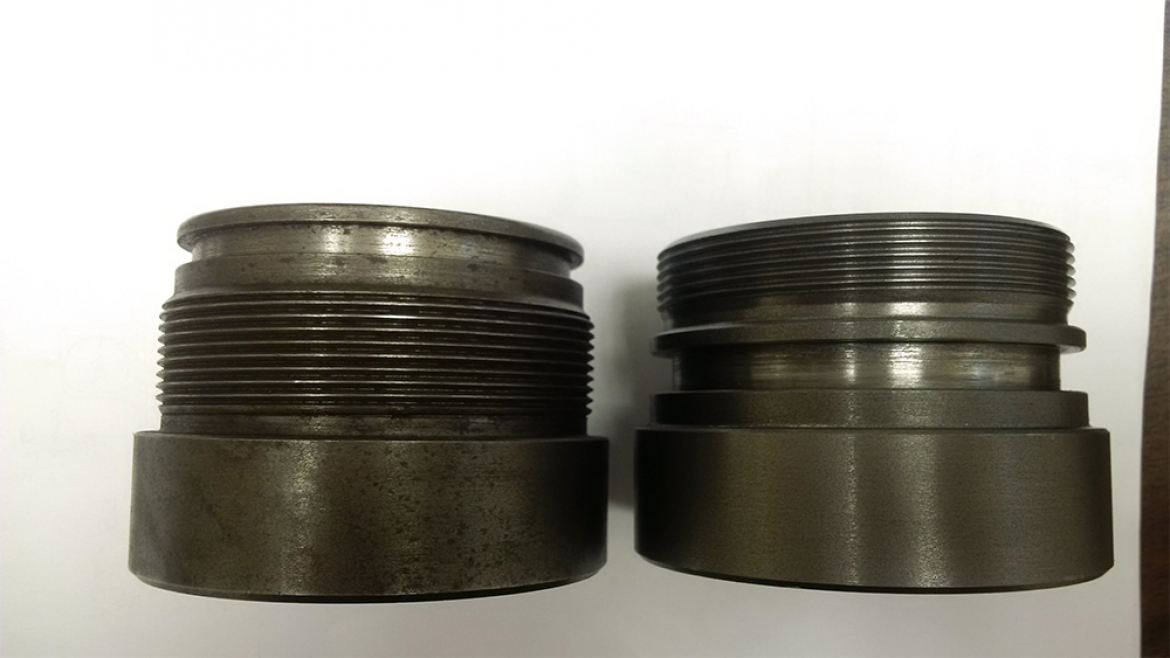 Two black metal fittings on a white surface in a machine shop.