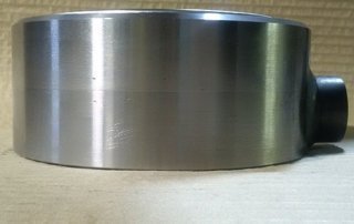 A stainless steel cylinder used for hydraulics on a table in a machine shop.